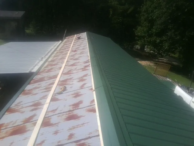 Old rusted panels beside newly installed green metal roofing — Wind Damage Roof Repair by Roofing Brothers in Eastport